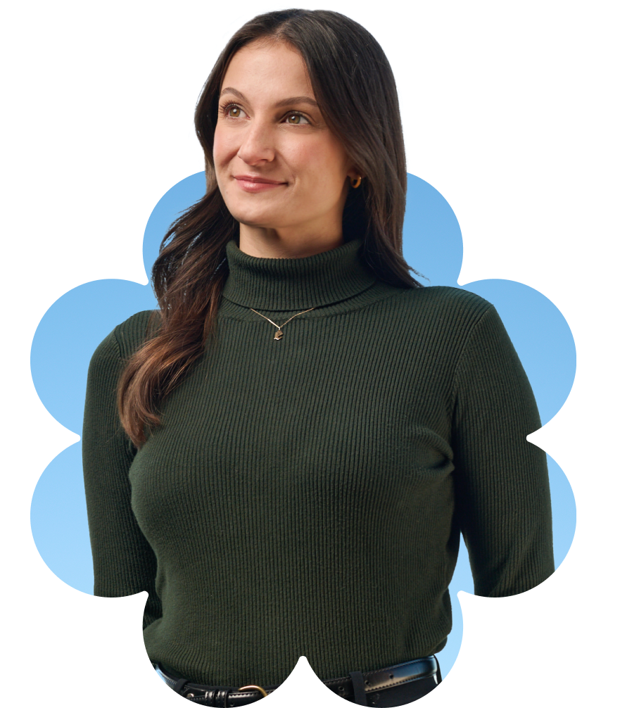 A woman with long brown hair, wearing a dark green ribbed turtleneck sweater and a gold necklace, stands against a blue background with a flower-shaped border. She is looking slightly to the side and smiling softly.