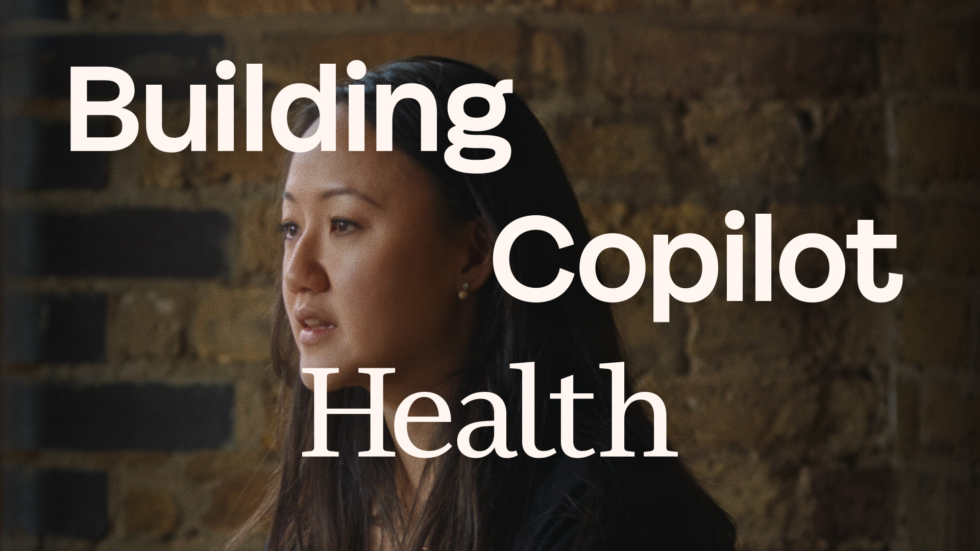 A woman with long dark hair sits in front of a brick wall. Overlaid white text reads: “Building Copilot Health.”.