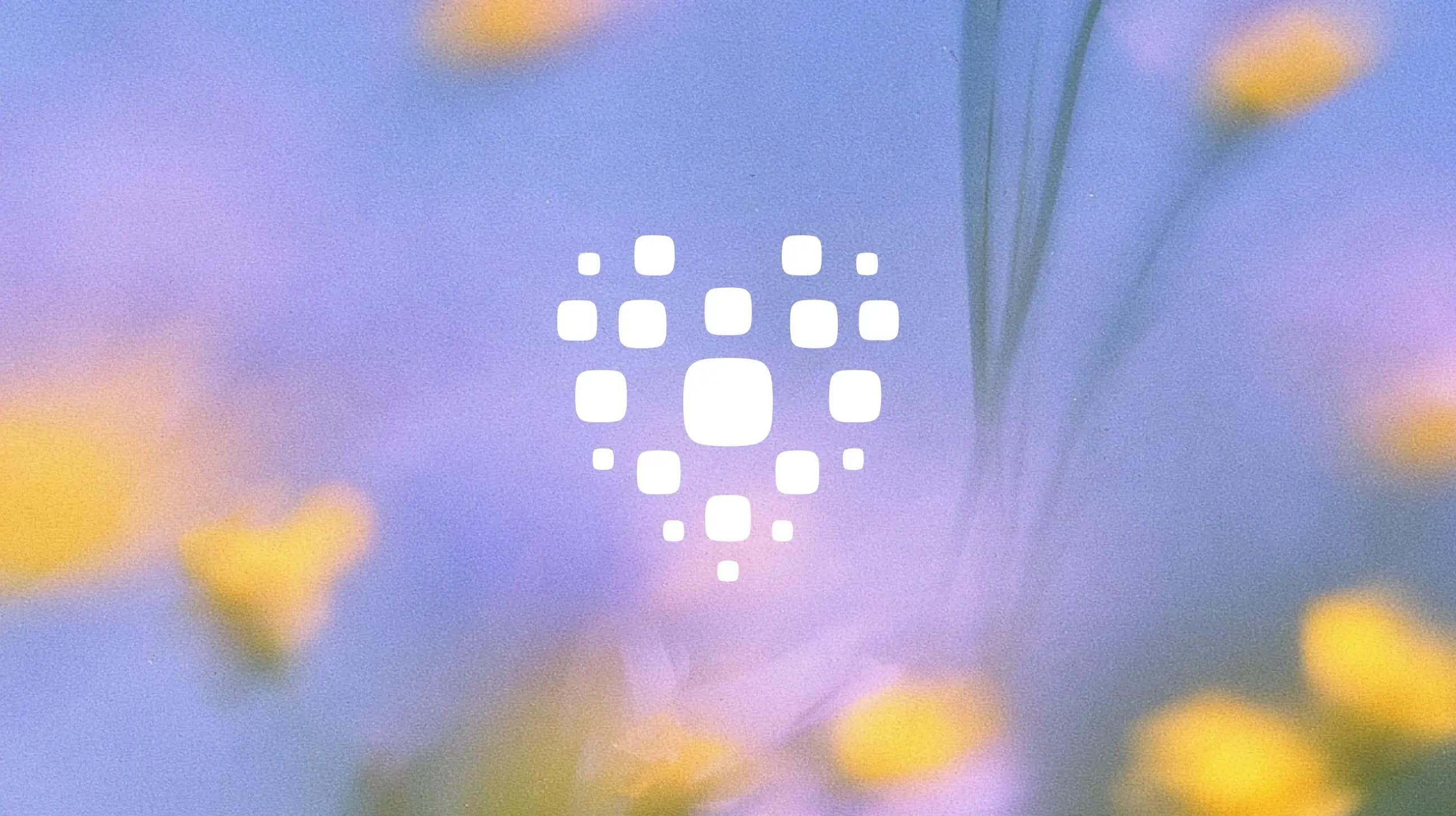A white heart icon composed of rounded square dots, centered against a blurred, colorful floral background.
