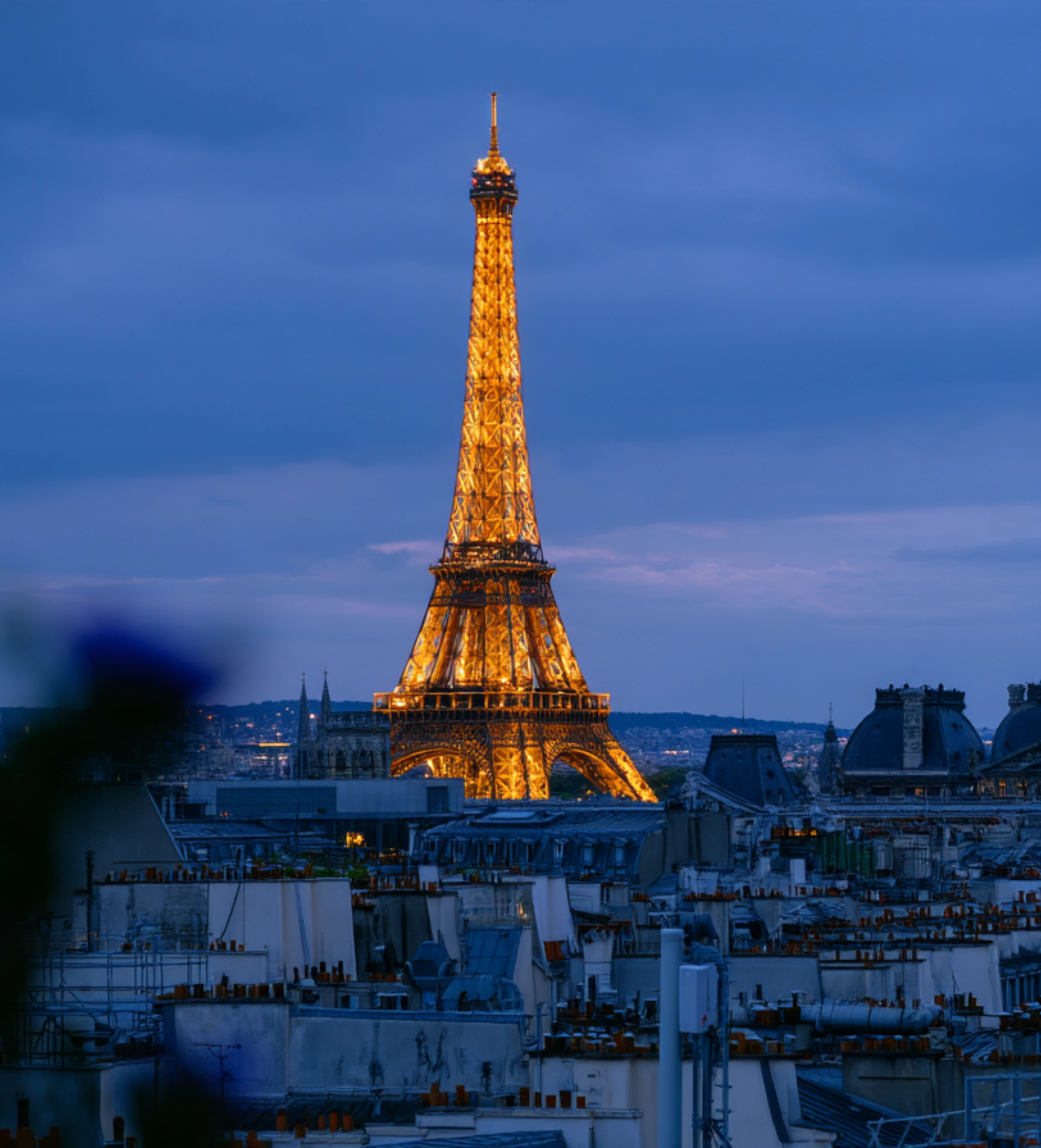 The Eiffel Tower illuminated at night, towering over the rooftops of Paris.